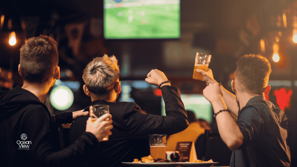 A group of diverse people cheering enthusiastically while watching a game on large screens.